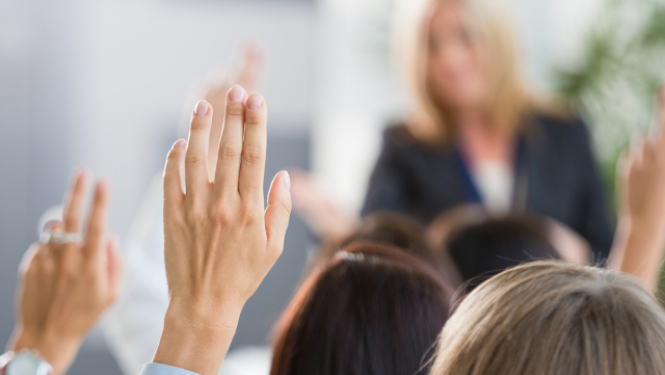 Skolēni paceļ rokas klasē, piedaloties mācību stundā.