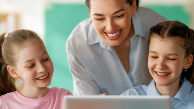 Skolotāja kopā ar bērniem skatās mācību saturu datorā.