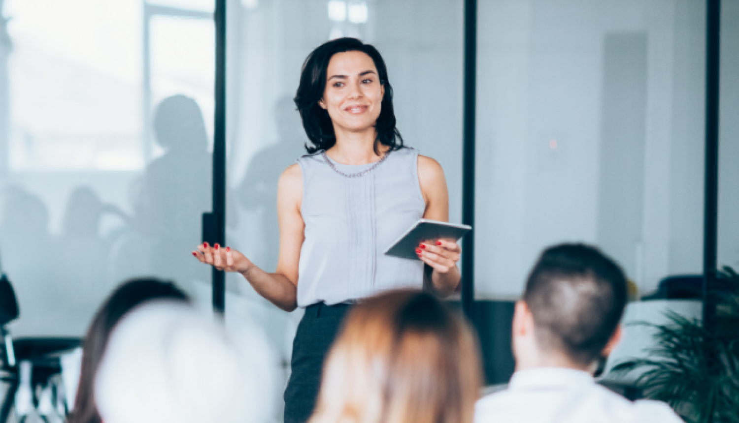 Skolotāja stāv auditorijas priekšā un uzrunā klātesošos