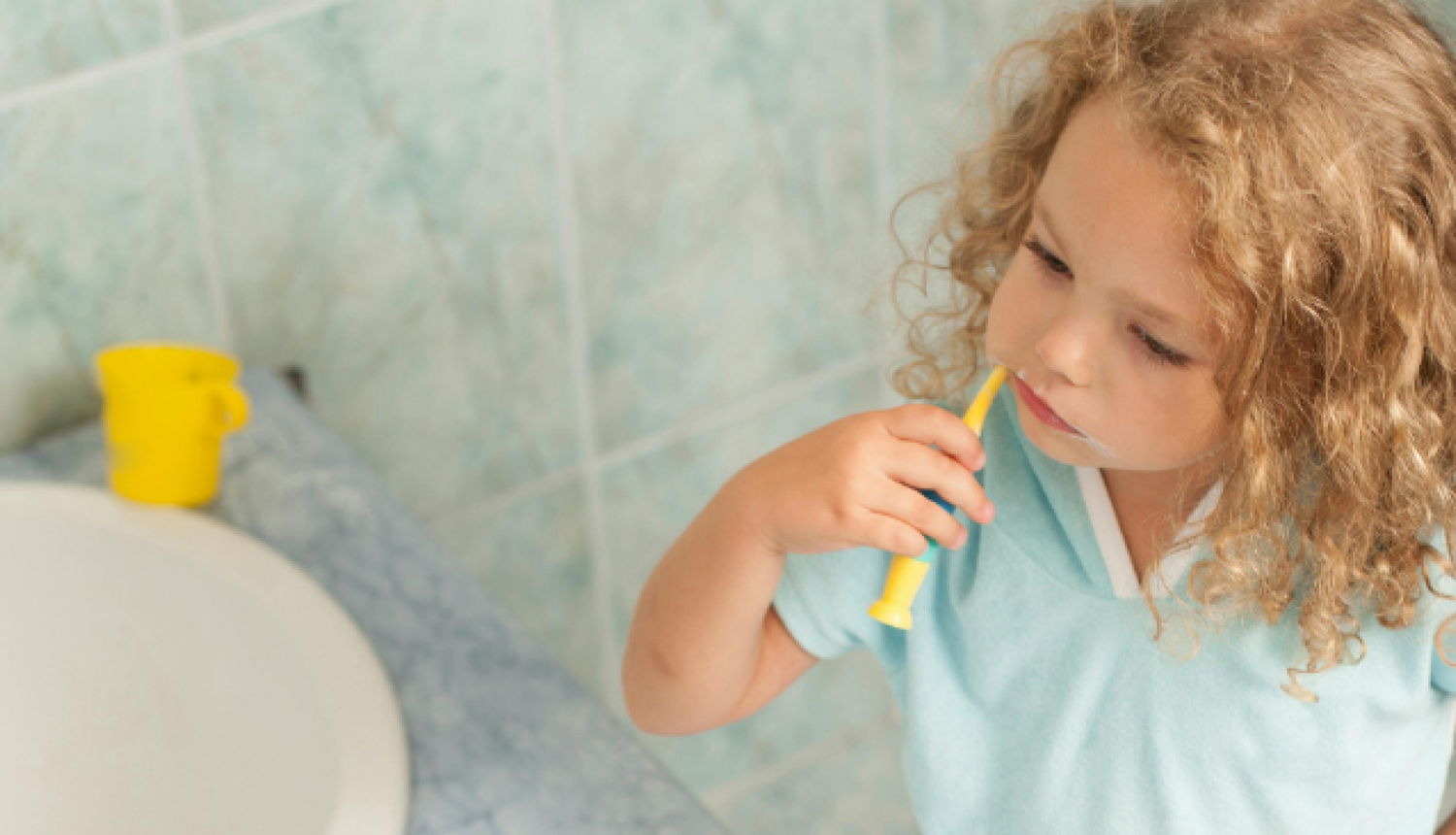 Mazs bērns vannasistabā tīra zobus pie izlietnes.