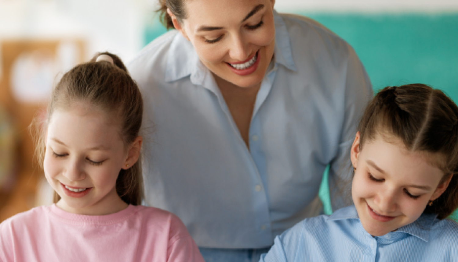 Skolotāja palīdz bērniem pildīt rakstīšanas uzdevumus pie galda.