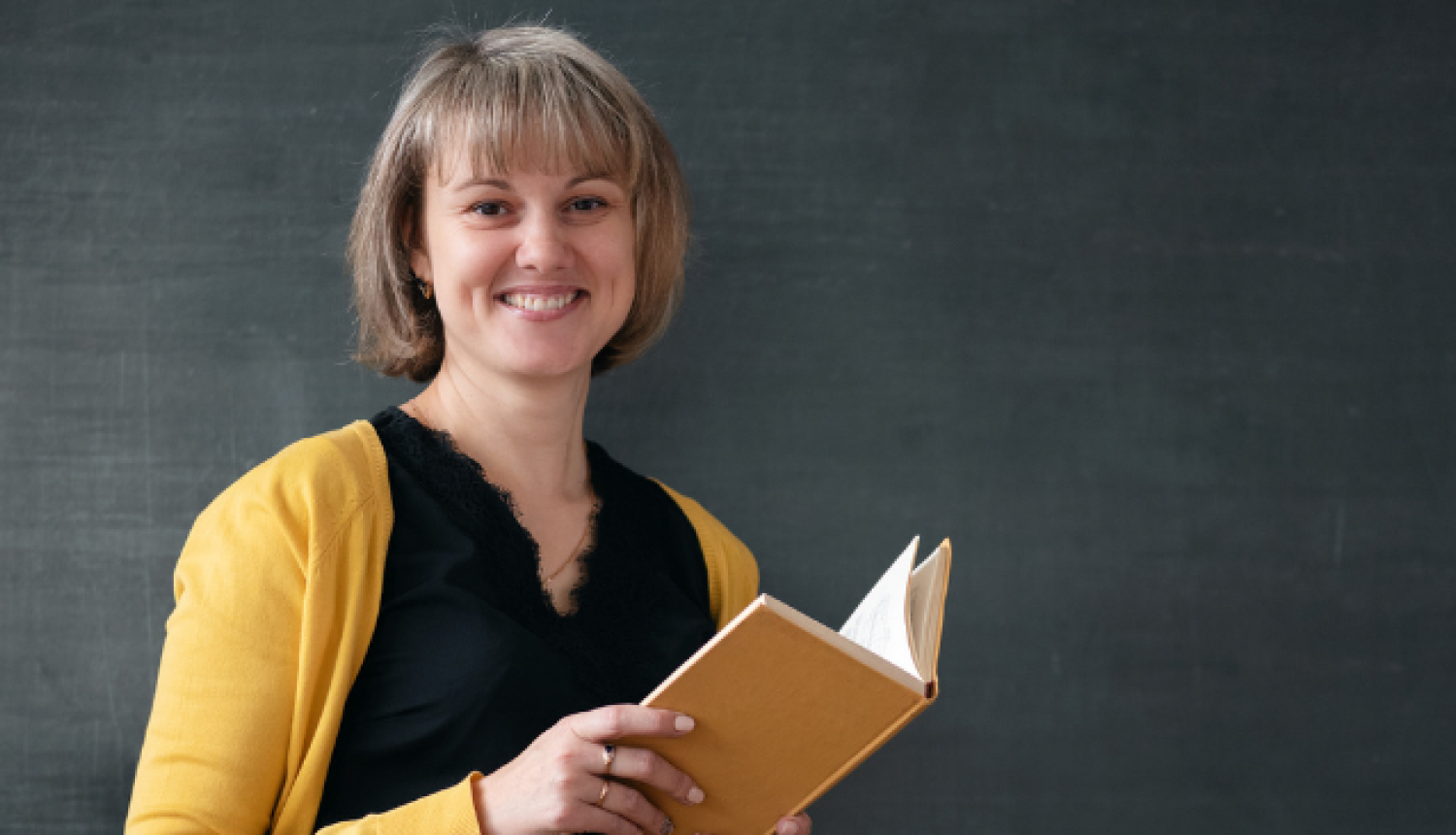 Skolotāja stāv klases priekšā un lasa grāmatu.