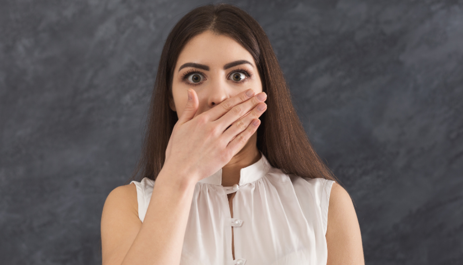 Pārsteigta sieviete ar roku aizklātu muti.